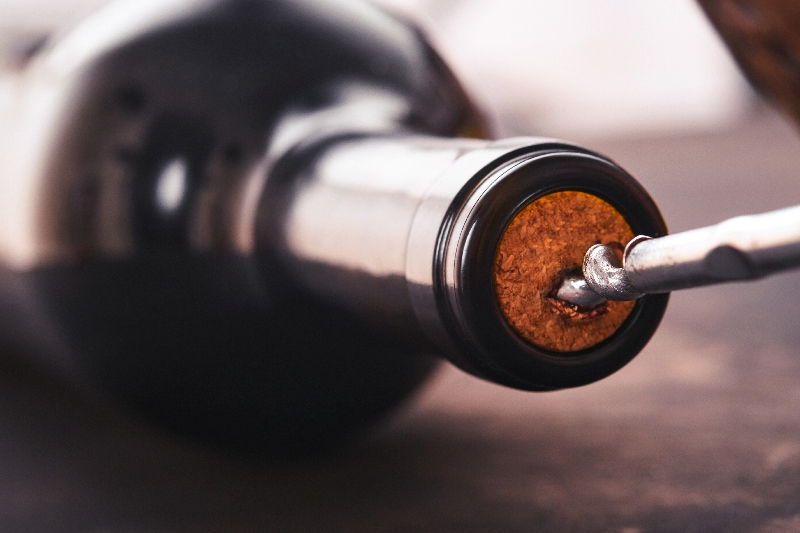 Bottle wine with corkscrew. Opening a wine bottle with a corkscrew in a restaurant. Wine composition on dark rustic background with copy space. Mock up.
